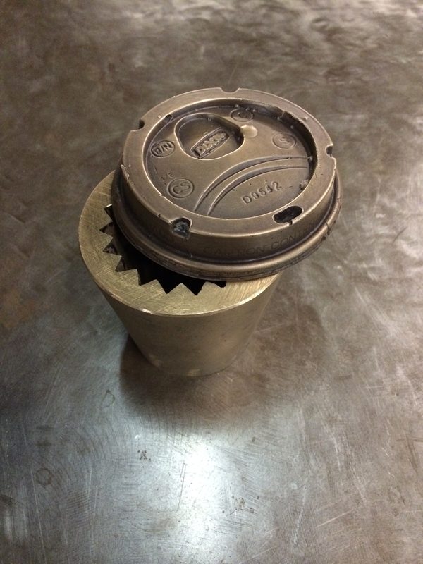 Cast bronze takeout coffee cup with a gear-toothed interior and a cast lid, on a steel table